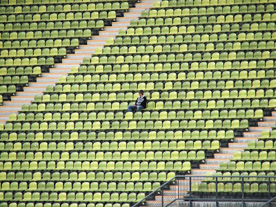 Single white male sitting alone in a stadium full of green chairs